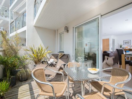A balcony with chairs a table and plants overlooking an apartment living room at Clearwater in St Ives