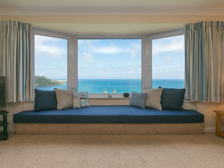 A sitting area with cushions in front of a large bay window overlooking the sea at Dolphin Watch in Carbis Bay
