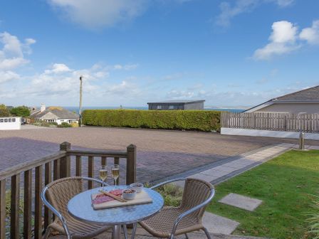 A small outdoor seating area with a round glass table two chairs and snacks on the table overlooking a paved area with hedges and houses in Gennaker Carbis Bay