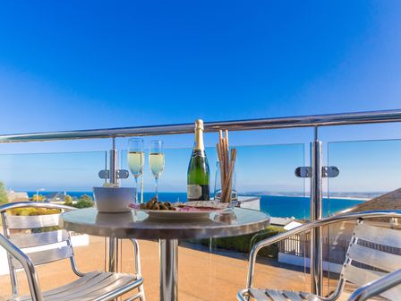 A balcony with a round table set with champagne, glasses, and snacks overlooking the sea at Genoa in Carbis Bay