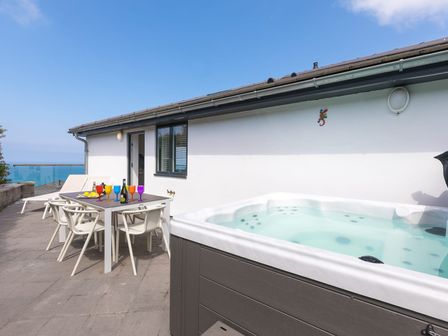 An outdoor patio with a hot tub table with colorful glasses chairs and loungers by a house at Gwel An Godrevy in Carbis Bay