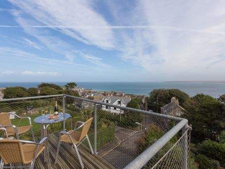 A balcony with a table set with a bottle and glasses overlooking a coastal town and sea at Gwel an Mor in St Ives