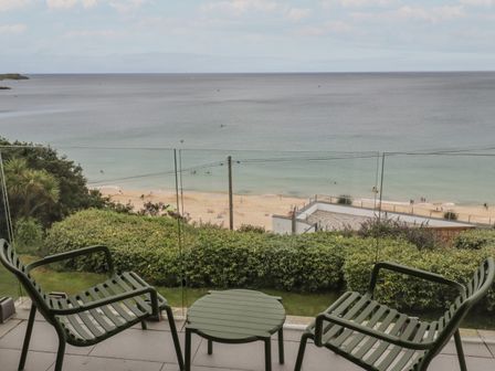 A balcony with two chairs and a table overlooking a beach and the ocean at Halfway Tree in Carbis Bay