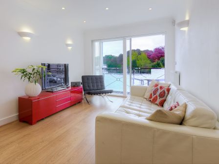 A living room with a white sofa and red cabinet with a tv and sliding glass doors showing a balcony and trees at Indigo St Ives