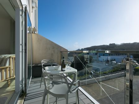A balcony with a table set with a bottle and glasses overlooking buildings and hills at Ithaca in St Ives