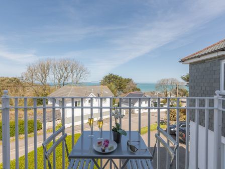 A balcony with a table and chairs overlooking houses and the sea at Kerensa in Carbis Bay