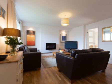 A living room with two leather sofas a wooden coffee table a television a lamp and flowers on a sideboard at Pentreath in Carbis Bay