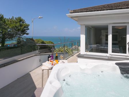 An outdoor deck with a hot tub a small table with drinks and snacks and a view of the sea at Portside in Carbis Bay