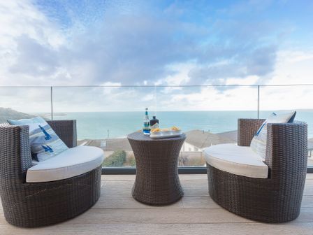 A balcony with two wicker chairs and a small wicker table overlooking the ocean at Sandsifters III in Carbis Bay