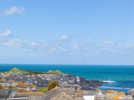 A coastal town with houses and a grassy hill near the ocean at SeaMore in St Ives