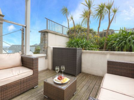 An outdoor seating area with two cushioned wicker sofas a wicker table with food and drinks and plants behind a railing at Serendipity in St Ives