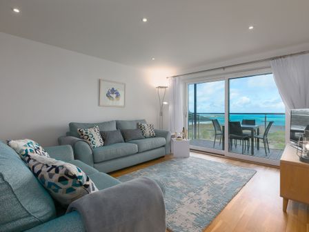 A living room with blue sofas a patterned rug and a view of the sea through sliding glass doors at Silver Sands in Carbis Bay