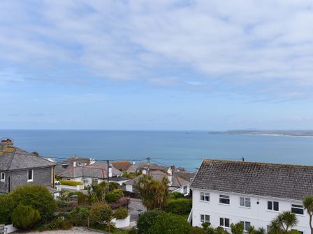 A coastal view over houses and trees with the ocean and sky in the background at St Ives Bay View in Carbis Bay