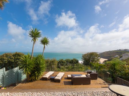 An outdoor wooden deck with lounge chairs and a seating area overlooking the ocean at The Breakers in Carbis Bay