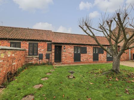 A brick cottage with a tiled roof a grass lawn a stone path and a tree at Well Cottage in Leven Near Beverley