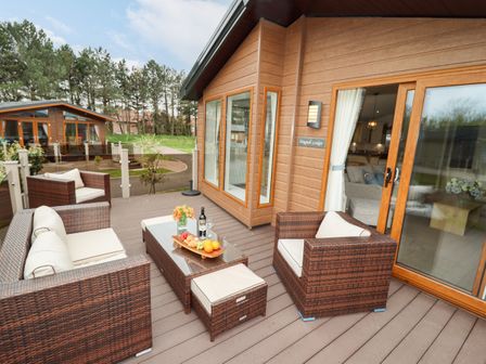 An outdoor deck with wicker seating and a table with fruit and wine at Seagull Lodge in Runswick Bay