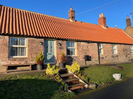 A stone house with a red tiled roof and green door with steps and plants in front at Woolley Lodge in Wooler