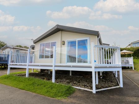 A small house with white railing around a raised deck and sliding glass doors at The Potting Shed in New Quay