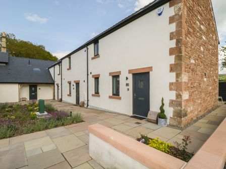 A paved pathway and flowerbed outside a building with white walls and stone corner at Tarn End Cottages 12 Talkin near Brampton Cumbria