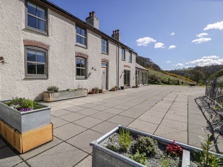 The exterior of a house with a large paved patio and several planter boxes with plants at Fron Goch Farm Llanfair Talhaiarn