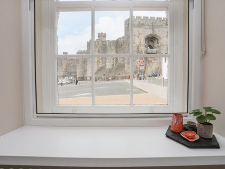 A window with a view of a stone castle with small ceramic pots and a plant on the windowsill at Nantlle in Caernarfon