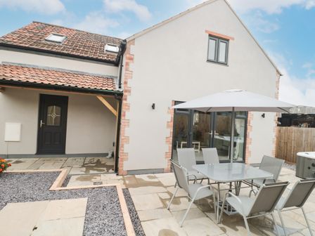An outdoor patio area with a glass table and six chairs under an umbrella next to a modern house at Bramley Cottage Henley near Langport