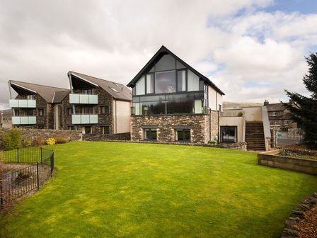 A modern stone and glass house with a large lawn and neighboring buildings at Carus House at Carus Green Golf Club Kendal