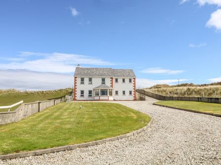 A two story house with a gravel driveway and lawn under a blue sky at Realt na Farraige in Derrybeg County Donegal