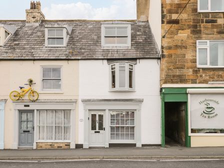 A street view of two houses with grey doors and windows and a yellow bicycle mounted on the wall next to a Harbourside Tea Room in Whitby