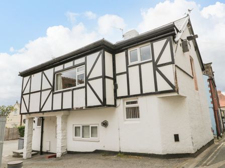 A two-story house with black wooden beams on white walls and white pillars at Daisy's Den in Whitby