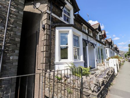 A row of stone terraced houses with white framed windows and small front gardens along a sidewalk at 8 Waterhead Terrace in Ambleside