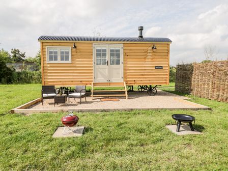 A wooden cabin on wheels with outdoor chairs and tables in front and two fire pits on grass at Waylands in Uffington