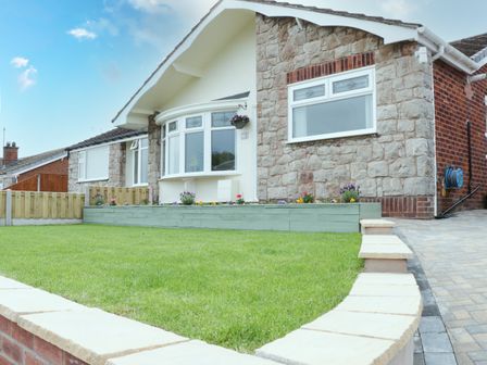 A front yard with green grass a raised flower bed and a stone house with windows at Bryn Hafod in Deganwy