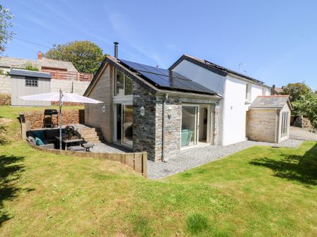 A stone and white exterior house with solar panels and a lawn with an umbrella and outdoor seating at Kelmscot in Trelights
