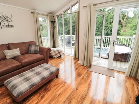 A living room with a brown sofa and plaid ottoman next to glass doors leading to a balcony with outdoor chairs and a hot tub at Number 43 Burnside Lodge in Felton