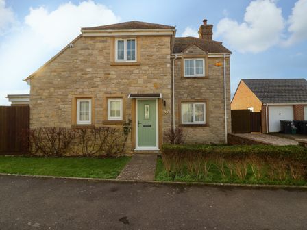 A stone house with a green front door four windows a grass lawn and a paved pathway at West Bay Holiday Home in West Bay