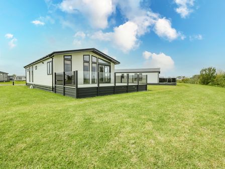 A static caravan on a grassy plot with a glass-paneled deck at Fairway View 24 in Brean