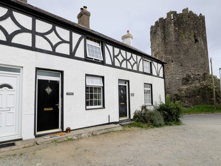 A white building with black doors and windows next to a stone tower at Y Bwthyn in Conwy