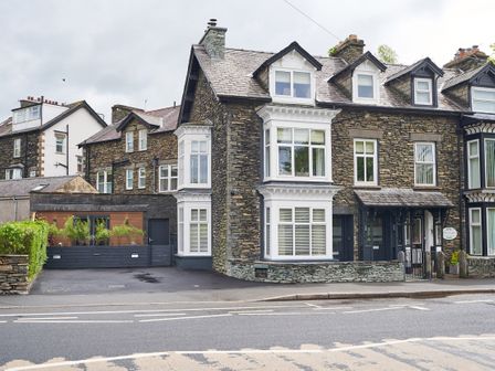 A stone building with multiple white bay windows and a driveway at Lower Sheriff's Place in Windermere