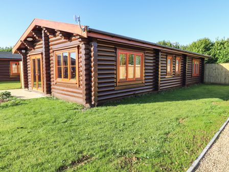 A wooden log cabin with multiple windows and a glass door on a grassy lawn at Holly Lodge in Greetham Rutland