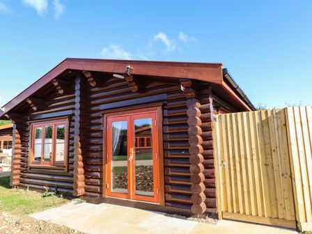 A wooden log cabin with double glass doors and a window next to a wooden fence at Pine Lodge in Greetham Rutland