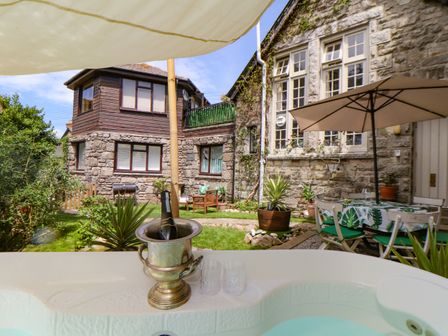 An outdoor garden area with a hot tub champagne bucket table with umbrella chairs and stone building at Roncon's Villa in Goldsithney