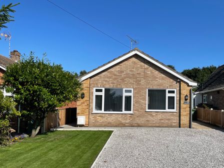 A single-story brick house with two windows and a graveled driveway with a lawn and tree at Harbour Place in Wells-Next-The-Sea