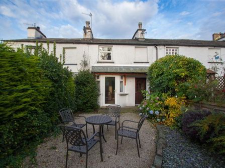 An outdoor patio area with a metal table and four chairs surrounded by bushes and plants at Rustic Cottage in Bowness-On-Windermere