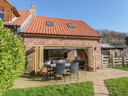An outdoor patio with a table and chairs in front of a brick house with open folding doors and a tiled roof at Kaitkyella Lodge in Scarborough