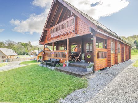 A wooden cabin with a porch and outdoor seating on a grassy lawn at Sun View Lodge in Llanbedr