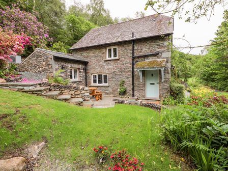A stone cottage with a garden and wooden picnic table in a rural setting at Silverthwaite Cottage in Skelwith Bridge near Elterwater