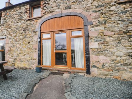 A stone house exterior with a wooden framed glass door and small window above at Daisy Cottage in Penruddock