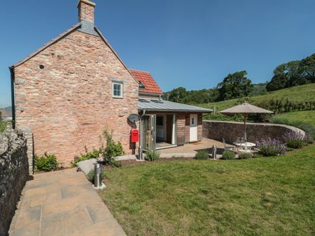 A stone cottage with a red mailbox patio table chairs and an umbrella in the garden at Lilac Cottage in Wookey Hole near Wells
