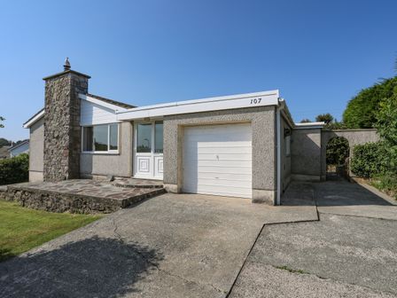 A single story house with a stone chimney a white garage door and a concrete driveway at Ty Bedw in Benllech